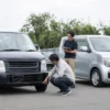 中古車販売店で年式の異なるワゴンRを比較し車体下部を確認する男性