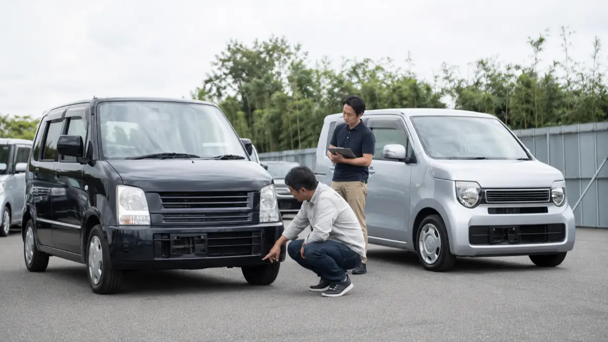 中古車販売店で年式の異なるワゴンRを比較し車体下部を確認する男性