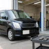 整備工場を背景にした黒いワゴンRとブレーキパッドなどの交換部品