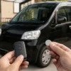 黒いワゴンRを背景にスマートキーと交換用ボタン電池を持つ手元