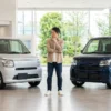 現行ワゴンRのZLとHYBRID ZXをイメージした2台の軽ワゴンを販売店で比較する日本人男性