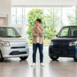 現行ワゴンRのZLとHYBRID ZXをイメージした2台の軽ワゴンを販売店で比較する日本人男性