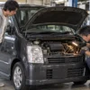 ボンネットを開けた黒いワゴンRの補機ベルト周辺を点検する日本人整備士