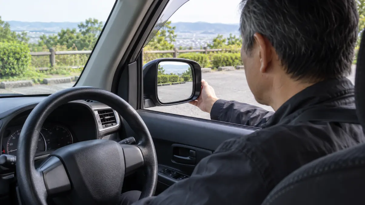 停車中にワゴンRの運転席側ドアミラーの固定状態と後方視界を確認する男性